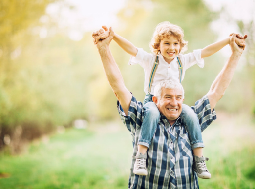 Older man carrying his grandchild on his shoulders representing primary care services for patients of all ages